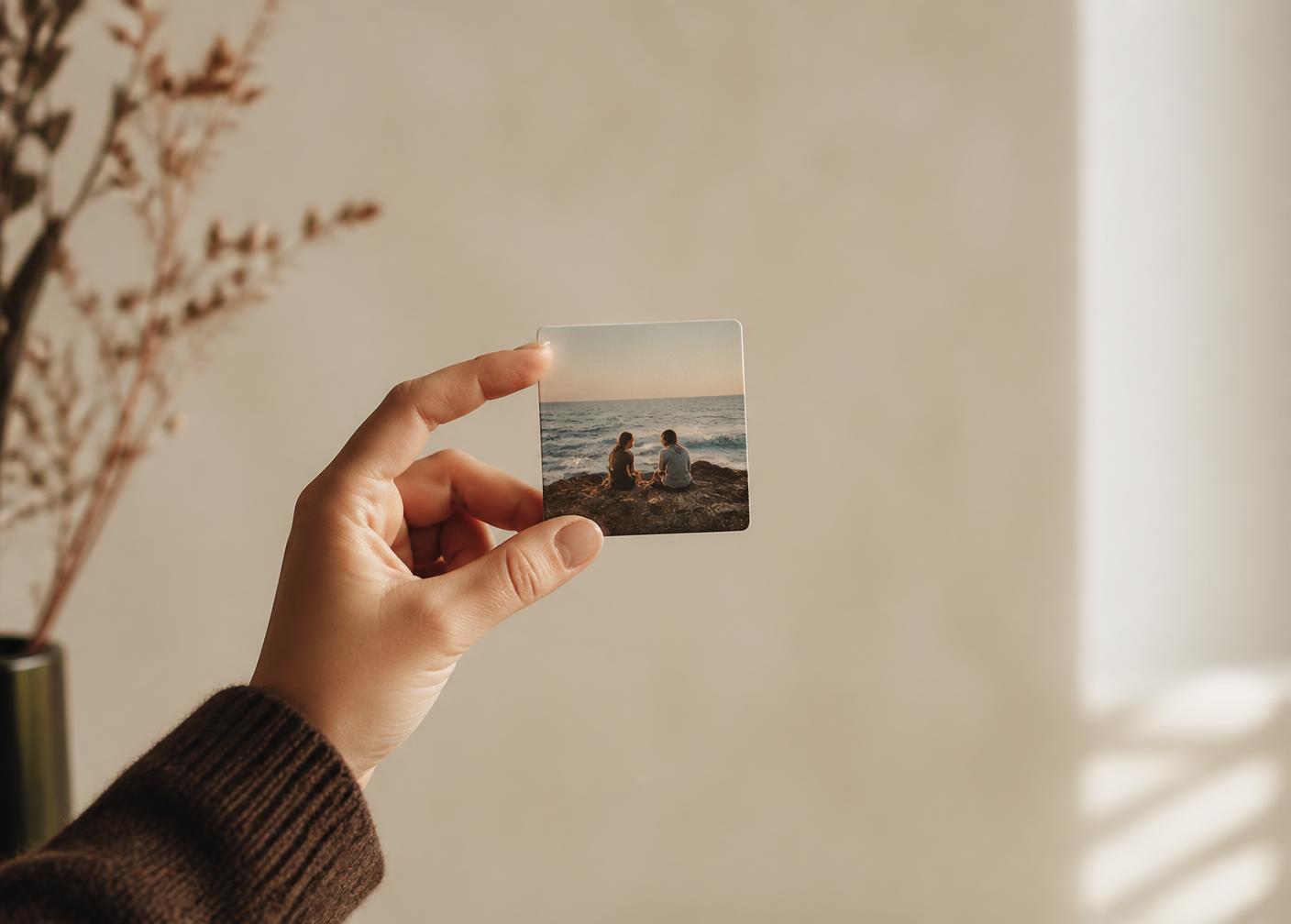 A hand holding a single square photo magnet